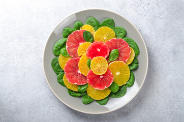 Salad made of orange and grapefruit slices and spinach leaves on a gray plate on light stone background. Top view, horizontal image