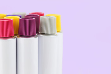 tubos de aluminio comprimible con tapones de rosca de colores en fondo lila con espacio para copia