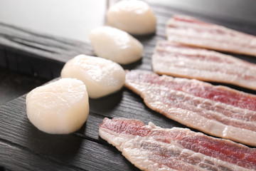 Wooden board with raw bacon and scallops, closeup