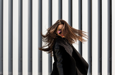 Lifestyle portrait of lovely young model in sunglasses with hair blowing in wind walking at the street