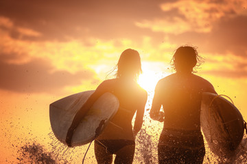 Couple of surfers run with boards and lots of splashes at sunset