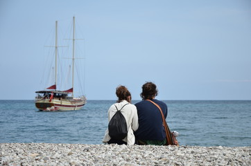 couple sitting at the beach on the background yacht