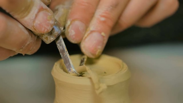 Professional male potter shaping and carving mug with special tool in pottery workshop, studio. Crafting, artwork and handmade concept