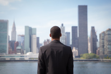 Fototapeta na wymiar Back view of ambitious young African American business man looking at NYC skyline, contemplating