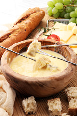 Gourmet Swiss fondue dinner on a winter evening with assorted cheeses on a board alongside a heated pot of cheese fondue with two forks dipping bread and white wine behind in a tavern