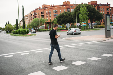 Boy walking by a pedestrian crossing with the phone - obrazy, fototapety, plakaty