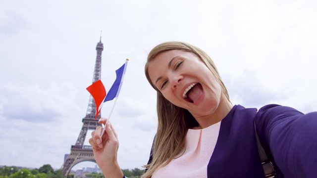 Woman with small French flag near Eiffel Tower in Paris, France doing selfie on mobile phone. Happy smiling tourist woman traveling in Europe.