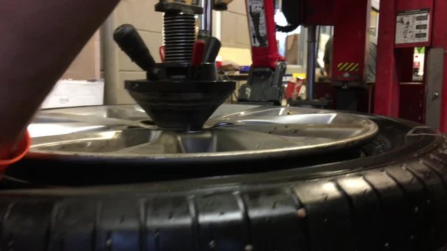 Close up of modern tire machine using inserted wedge to pry between rim and rubber while tire spins around before lifting it over rim.