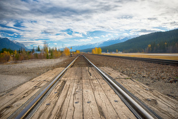 Fototapeta premium Railroad tracks in the horizon with the Canadian Rocky Mountains in the background, taken from Golden, BC