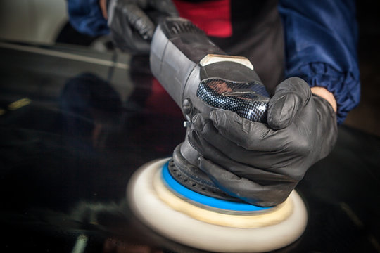 Close-up of a male mechanic with a blue prism and protective gloves will flicker the black metal bumper machine from small scratches after painting