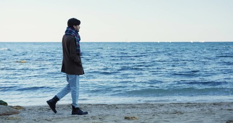 Handsome man walking on the beach across the sealine. Melancholic weather with cloudy sky. Sea horizont. Outside.