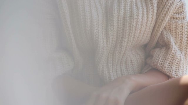Girl in a knitted sweater and bare feet sitting on the window, close-up.