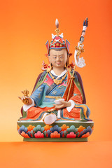 Figurine of Padmasambhava on an orange background.
