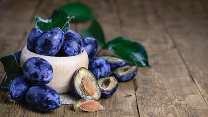 Blue plums with leaves on vintage wooden table.