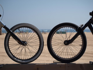 Two bicycle wheels facing in beach front