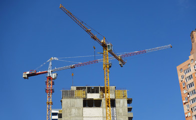 two cranes against the blue sky. construction of a multi-storey building