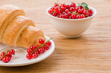 croissant and red currant in a white bowl/croissant and red currant in a white bowl on a wooden table. With copy space