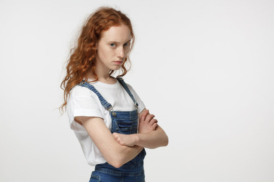 Indoor closeup photo of young good-looking redhead European teenager isolated on white background looking straight at camera having crossed arms being suspicious and not agreeing on common decision