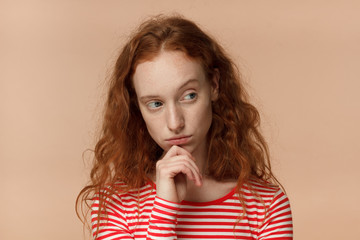 Closeup headshot of beautiful redhead woman isolated on peach background looking sidewards feeling...