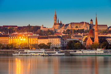 Budapest, Hungary - Golden hour in the morning with the Buda Castle, St. Matthias church and the Fisherman's Bastion with old ships on River Danube and clear blue sky - obrazy, fototapety, plakaty