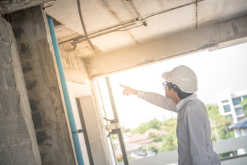 Naklejka na ściany i meble Engineer or Architect checking building while wearing a personal protective equipment safety helmet at construction site. Civil engineering, Architecture and building project concepts
