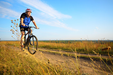 Fototapeta premium Male cyclist with backpack driving by rural dirt road outdoors