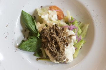 Warm salad with beef, tomato and lettuce leaves on white plate