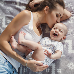 Young mother lying in bed with her newborn baby boy, playing together, happiness family concept, kid and mom bonding.Beautiful young mom looking at her baby son and smiling, lying in bed at home