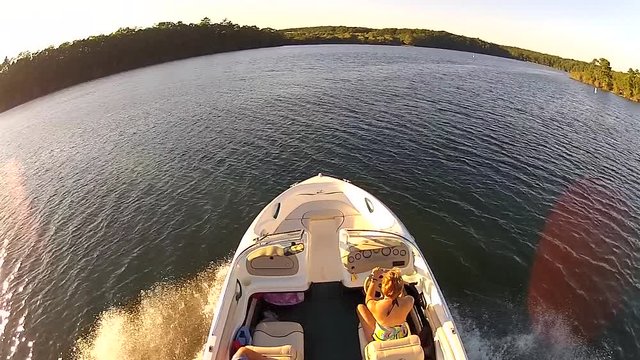 Riding along side speed boat on lake in summertime with woman driving