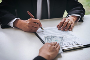 Bribery and corruption concept, bribe in the form of dollar bills, Businessman giving money while making deal to agreement a real estate contract and financial corporate