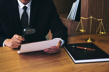 Male lawyer reading legal contract agreement and examining documents with magnifying glass in...
