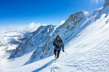 woman climber in helmet and down jacket with trekking sticks goes uphill at dawn