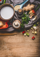 Obraz na płótnie Canvas Vegetarian Asian cuisine ingredients with chopped vegetables, coconut milk, seeds, spices and chopsticks on rustic wooden background, top view. Chinese or Thai food cooking