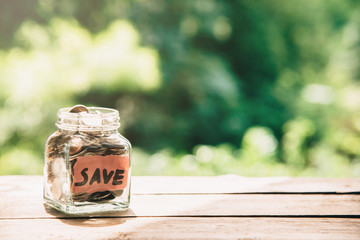 Coins in glass jar with the word save in front in natural sunlight .Saving money concept