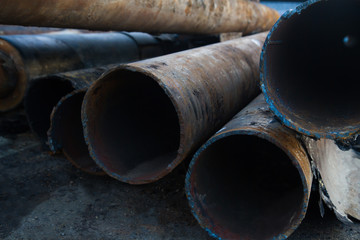 close up of a pile of large and rusting steel pipes lying on the  asphalt
