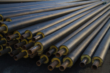 black steel pipe with heat insulation on the construction site in a plastic tube wrapper lying on...