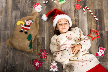 Adorable little girl wearing santa hat laying on wooden floor