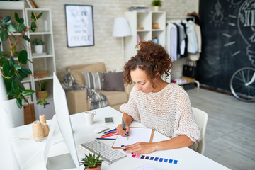 High angle portrait of modern creative woman working at desk choosing color palette for interior...