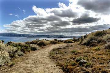Fototapeta na wymiar Road on the cliffs on the coast of La Coruna Bay (Galicia) on the Spanish Atlantic coast with the city of La Coruna in the background. Blue sky with some clouds and calm sea
