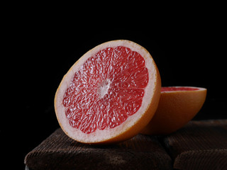 Grapefruit in a section on a black background. Sliced grapefruit on a wooden board, low key, dark background.