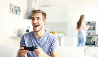 Man playing video games while his girlfriend cooking in the kitchen.