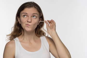 Young beautiful brunette girl cleans the ears with chopsticks with cotton wool and is surprised to get a lot of yellow earwax