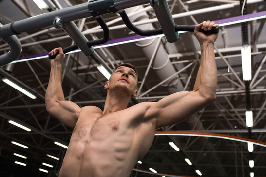 Low angle portrait of muscular young man with bare chest working out using machines  in modern gym against background on metal ceiling