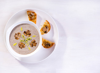 Soup with champignons, leek and crispy croutons on white background, top view.