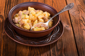 Stew with potatoes and meat in a ceramic plate on a wooden table.
