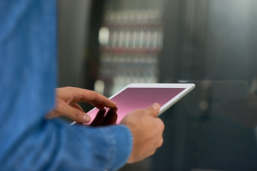 Closeup of systems administrator using digital tablet against bacground of server cabinet, copy space