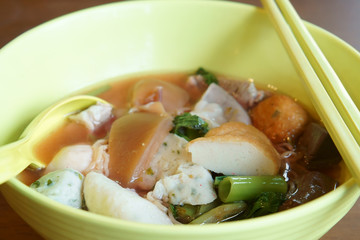 delicious yen ta fo seafood soup with noodles or pink and red noodle soup song kueng with fish ball and vegetable in yellow bowl with chopsticks and spoon on wood table for lunch at restaurant