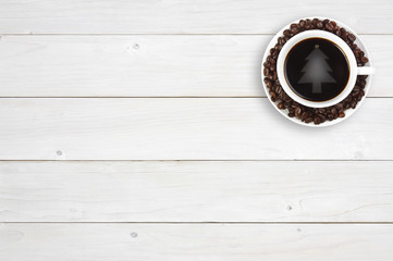 top view christmas tree reflective light on hot black coffee drink with beans in white cup on the corner white vintage wood table in cafe restaurant with copy space for your text or object