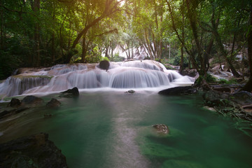 waterfall left side with clear green emerald water and rock for relax and refreshing cool with tree and root in the jungle or forest at Pha Tat waterfall for nature landscape background with sunlight