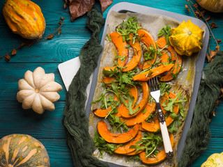 Baked pumpkin slices with arugula on baking tray. Fall food